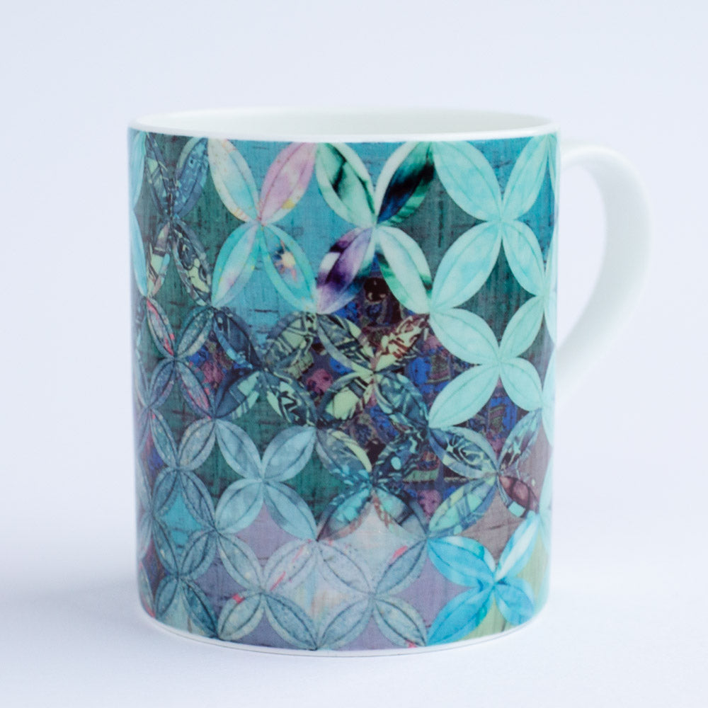 A patchwork quilt mug in green, teal and purple tones in a cathedral windows patchwork style