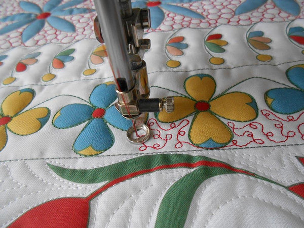 sewing machine needle with free motion foot sewing a curving and over lapping deisgn in red thread on white fabric areas surrounding printed flowers