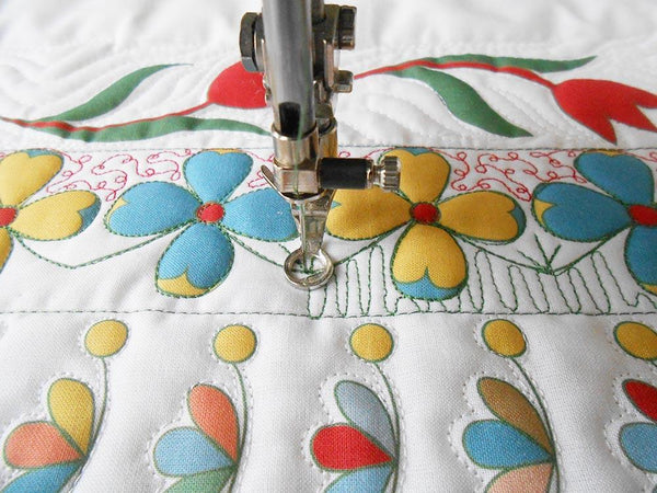 sewing machine needle with free motion foot sewing  an undulating wave design in green thread on white fabric areas surrounding printed flowers
