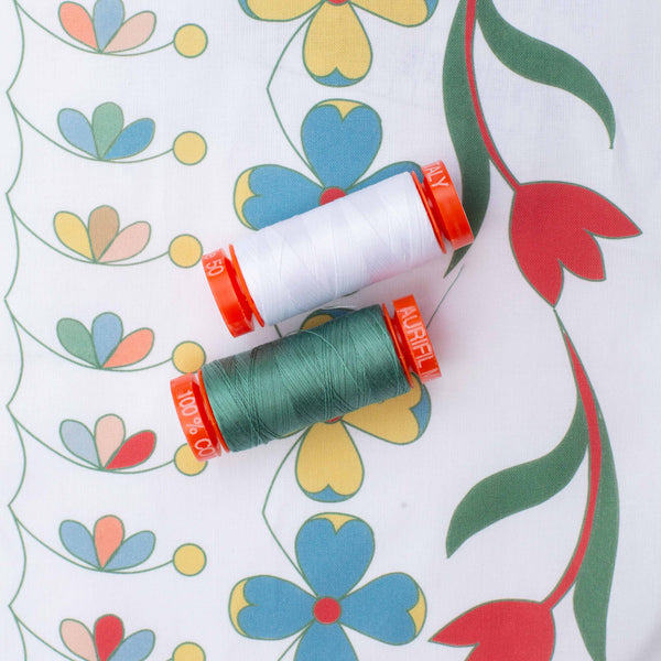 white and green spools of Aurifil sewing cotton on printed fabric